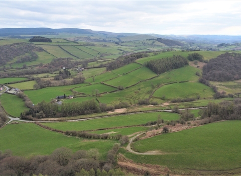 Aerial photograph of the Pentwyn Farm in Wales, showing rolling hills with patches of woodland and an overcast sky